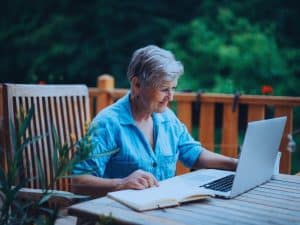 Transition to retirement strategies featured image showing a mature woman working on a laptop outside at home.